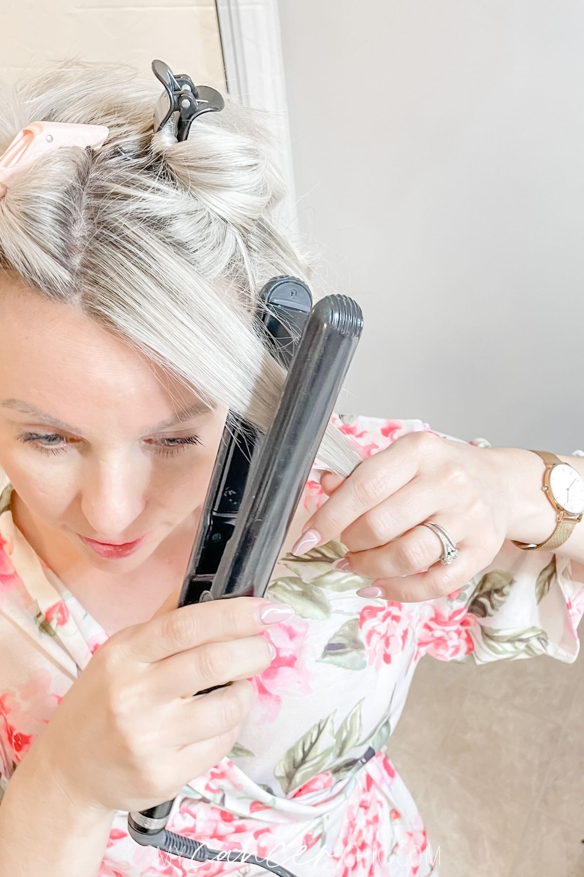 woman is using a flat iron to curl her short hair