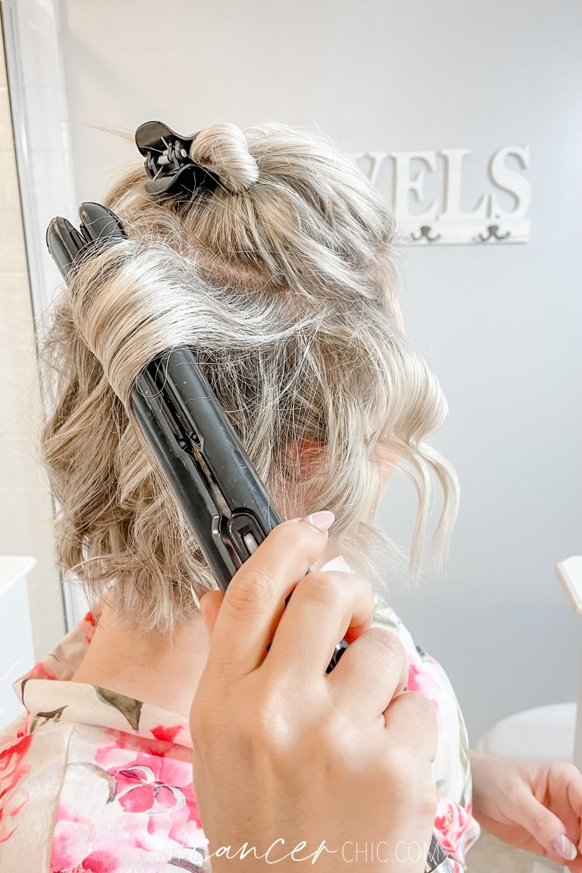 woman is using a flat iron to curl her short hair