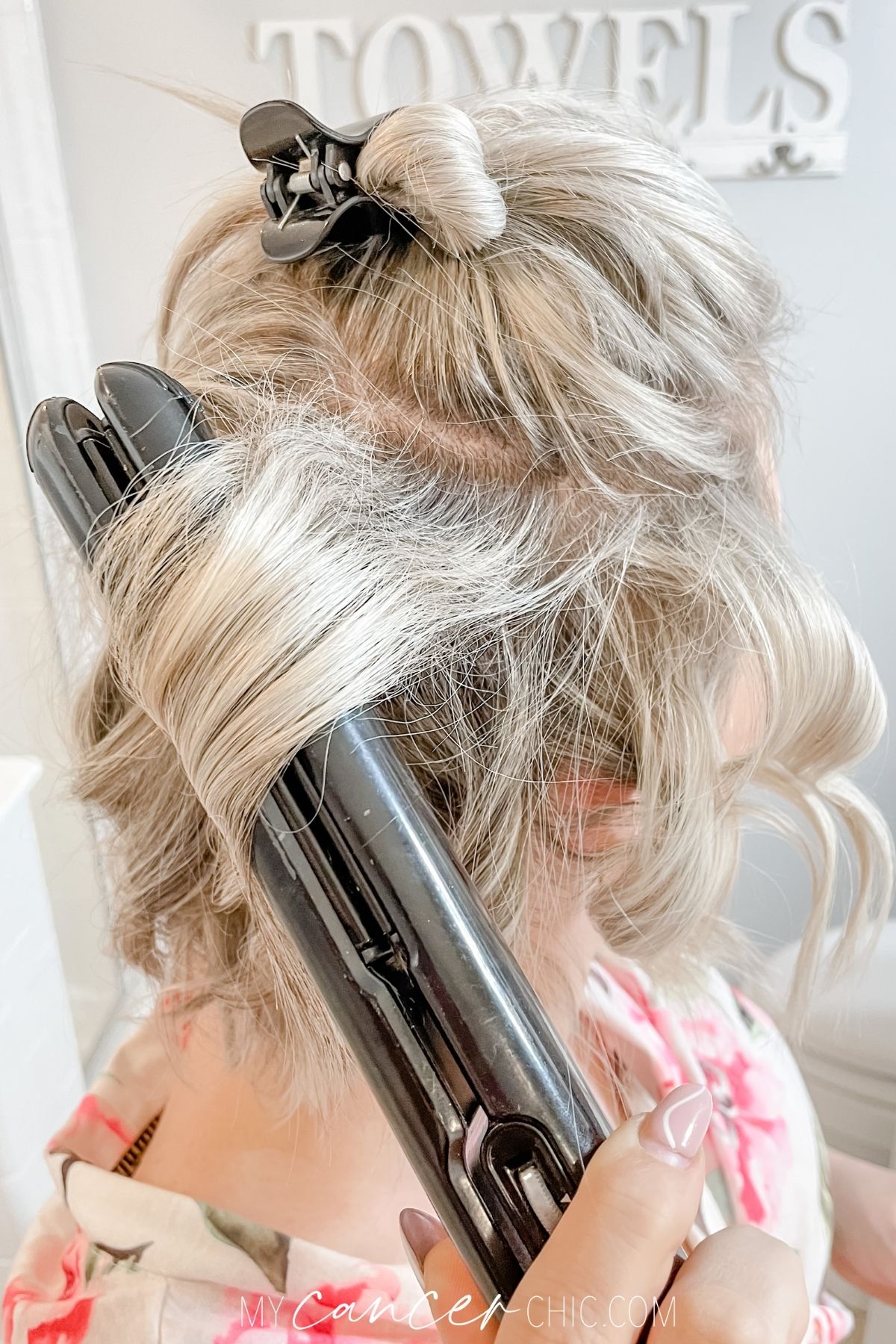 woman is using a flat iron to curl her short hair