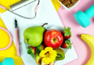 healthy living lifestyle changes after cancer fruits and dumbell and stethascope on pink and yellow background